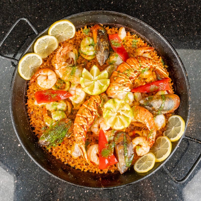 A large paella pan filled with seafood paella, garnished with lemon slices and red peppers.